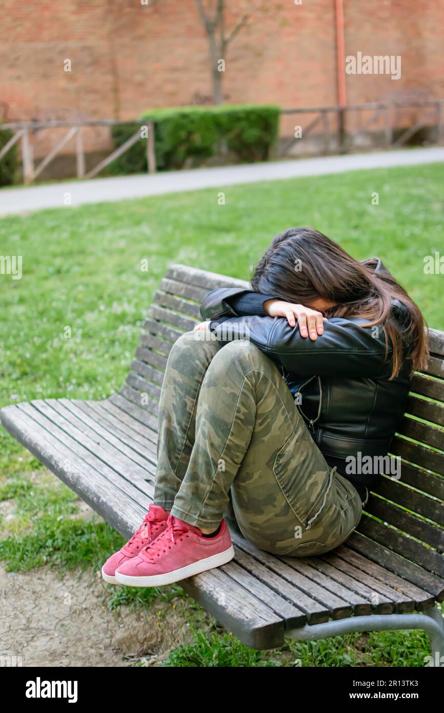 Junge Frau traurig und depressiv auf der Parkbank mit Armen und Kopf auf Knien Stockfoto