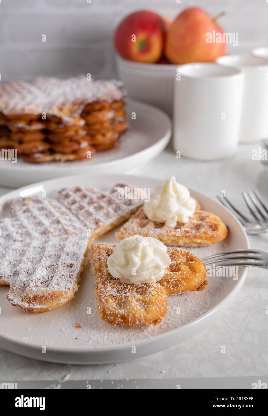 Frisch gebackene Waffeln mit Puderzucker und Schlagsahne auf dem Küchentisch Stockfoto