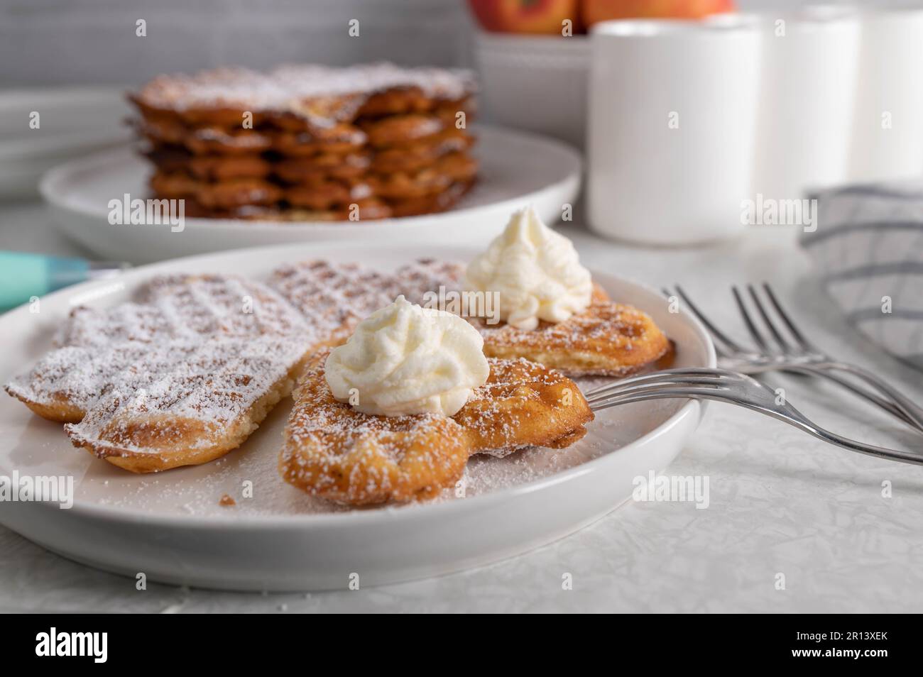 Frisch gebackene Waffeln mit Puderzucker und Schlagsahne auf dem Küchentisch Stockfoto