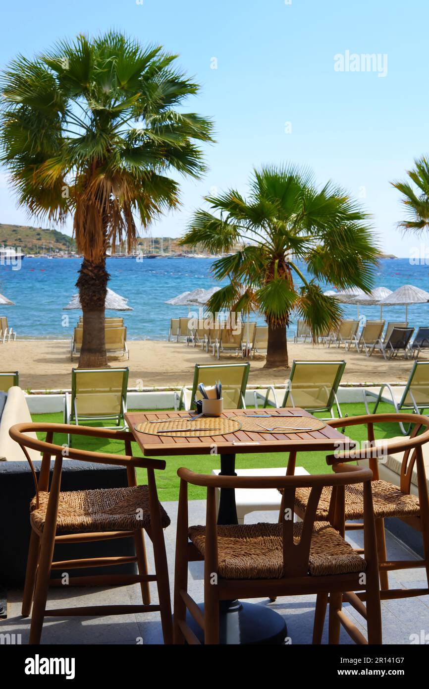 Tische im Restaurant mit blauem Meer und Palmen im Hintergrund Stockfoto