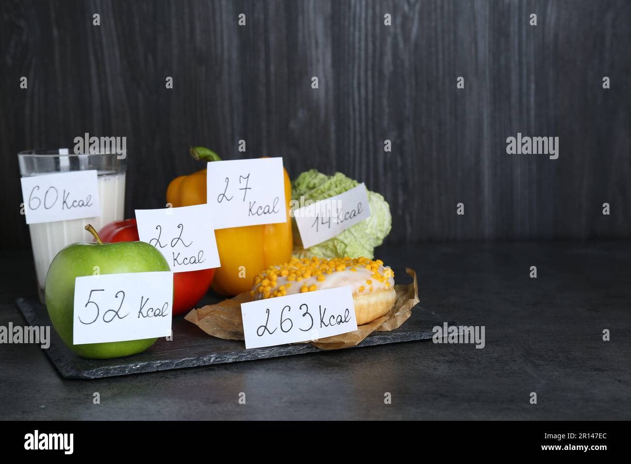 Lebensmittelprodukte mit Heizwert-Tags auf schwarzer Tabelle, Platz für Text. Gewichtsverlust-Konzept Stockfoto