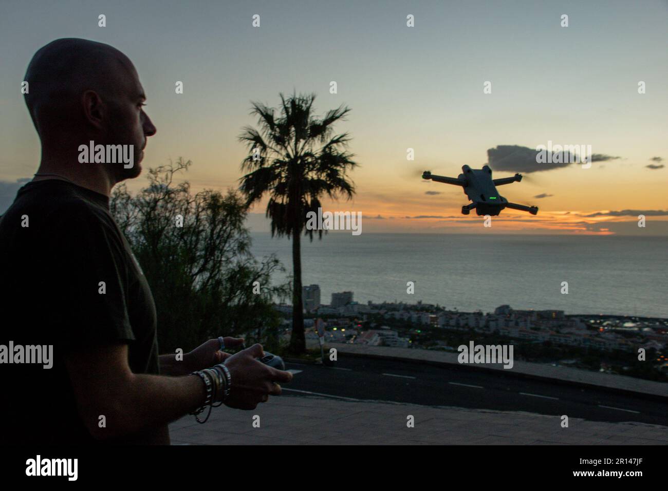 Ein weißer Mann kontrolliert seine Drohne bei Sonnenuntergang an einem tropischen Ort. Unbemannte Flugzeuge Stockfoto