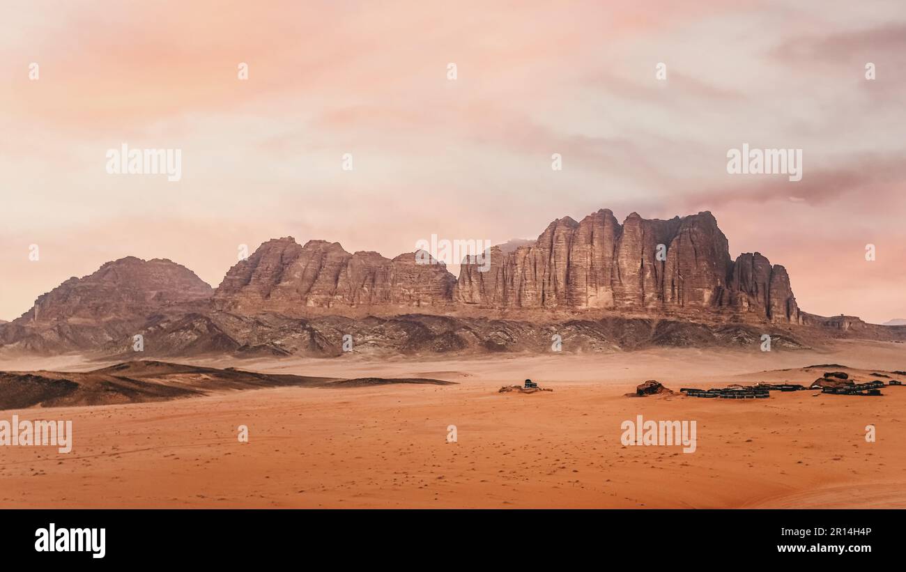 Felsige Landschaft in der Wadi Rum Wüste während des bewölkten Morgens, Zeltlager in der Ferne sichtbar Stockfoto