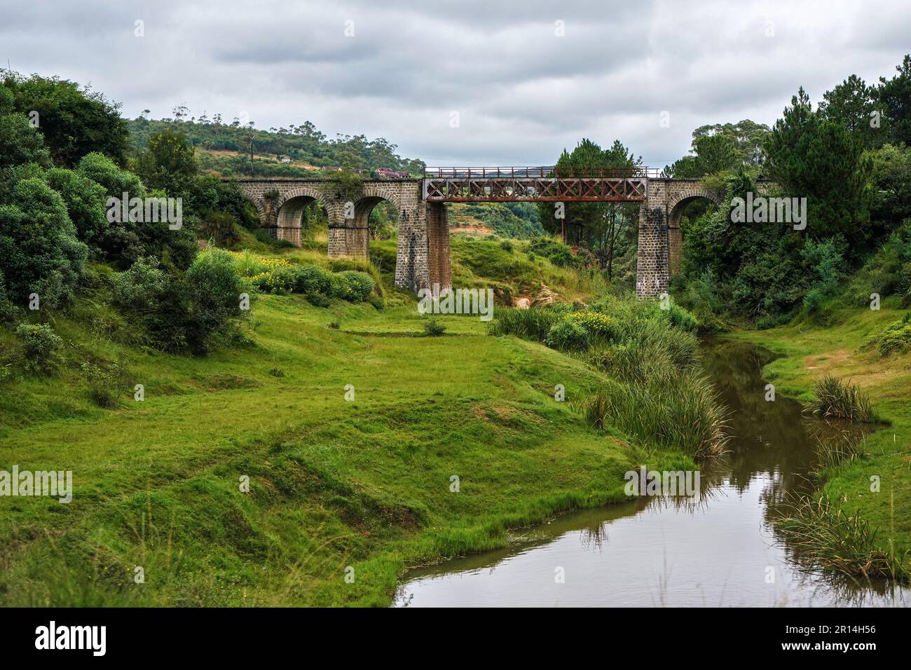 Kleine Eisenbahnbrücke über einen kleinen Fluss in der Nähe von Manjakandriana, Madagaskar, grünes Gras und Bäume. Insgesamt gibt es nur wenige Eisenbahnstrecken Stockfoto