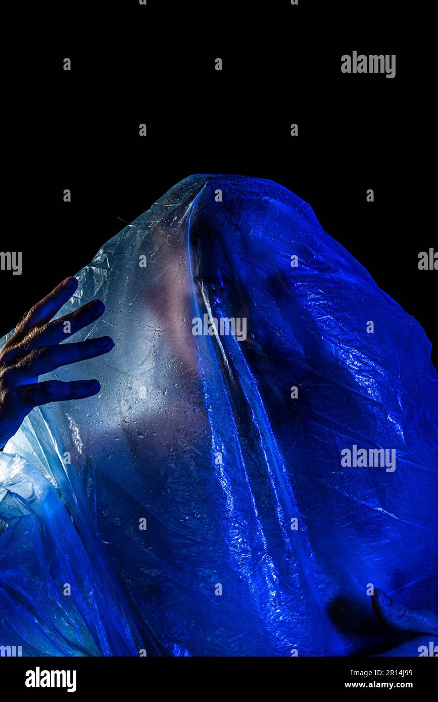 Mann mit Plastiktüte über dem Kopf, erstickt. Studioaufnahme mit blauem Filter. Isoliert auf schwarzem Hintergrund. Stockfoto