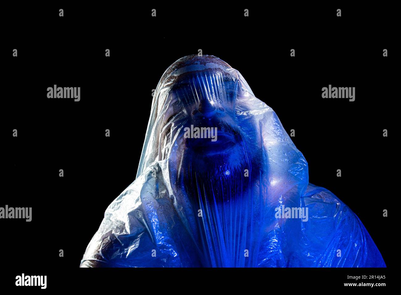 Mann mit Plastiktüte über dem Kopf, erstickt. Studioaufnahme mit blauem Filter. Isoliert auf schwarzem Hintergrund. Stockfoto
