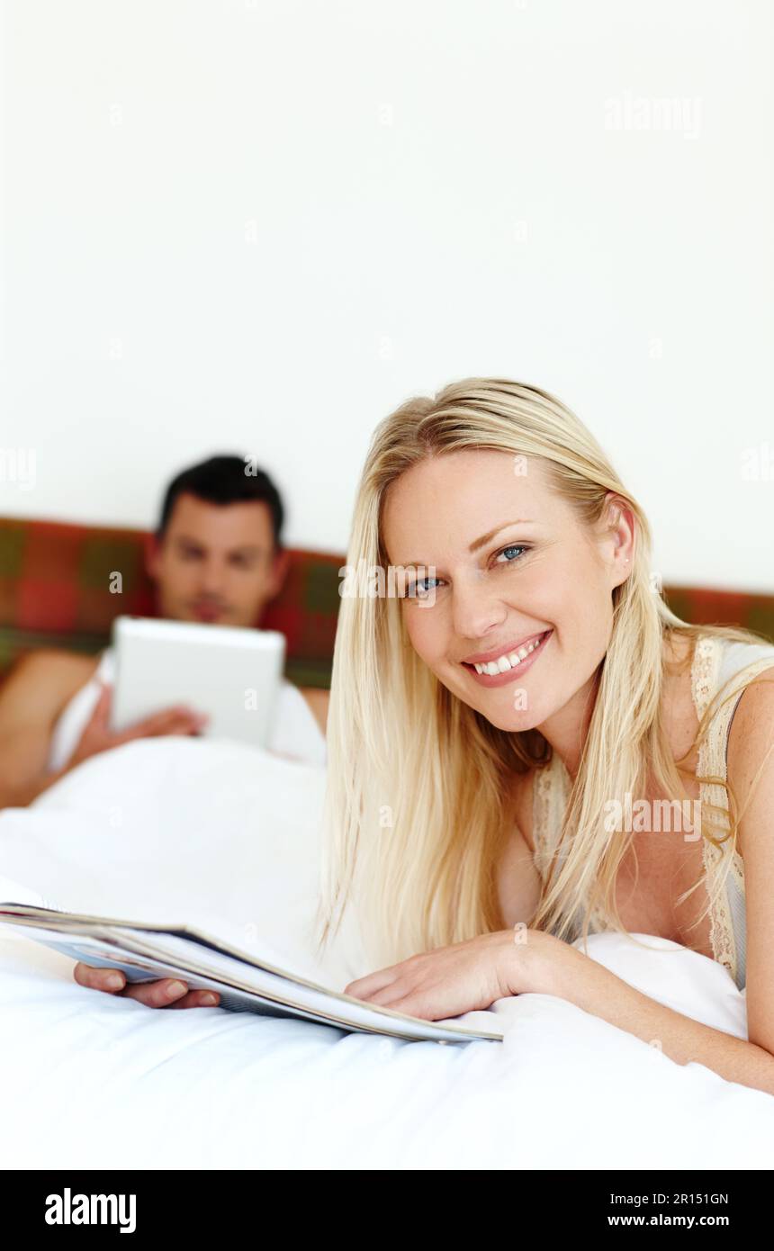 Ich liebe es, etwas Zeit mit meinem Mann zu verbringen. Porträt einer jungen Frau, die im Bett liest, während ihr Mann im Hintergrund liegt. Stockfoto