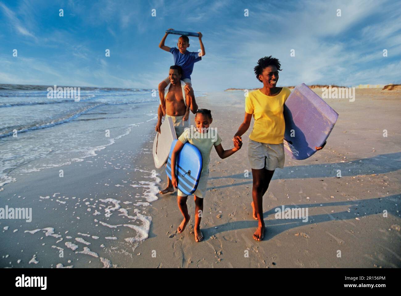 Afroamerikanische Familie mit Boogie Boards, die am Strand spazieren gehen Stockfoto