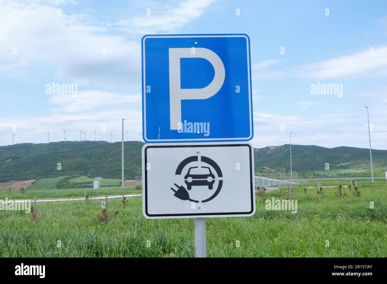 Schild mit Parkplätzen und Ladestationen für Elektroautos mit grünem Bereich und Himmelshintergrund. Stockfoto