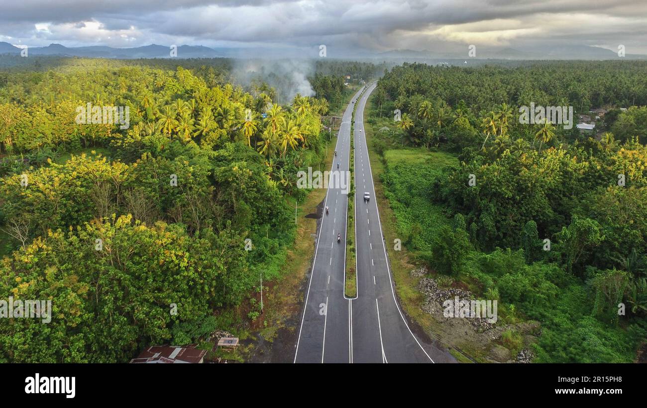 Luftfoto der Autobahn, die den Wald und Dörfer mit Berghintergrund trennt. Stockfoto
