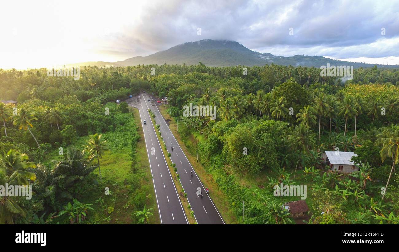 Luftfoto der Autobahn, die den Wald und Dörfer mit Berghintergrund trennt. Stockfoto