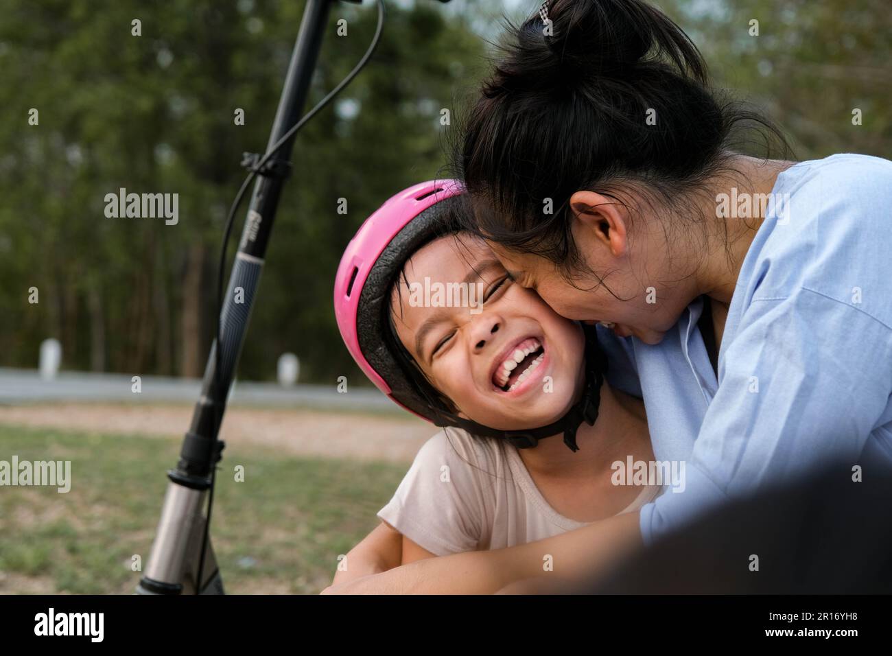 Mutter und Kinder sitzen und ruhen sich aus, nachdem sie mit dem Motorroller im Park gefahren sind. Mutter und Töchter verbringen ihre Freizeit gemeinsam mit Motorrollern im Freien. Happ Stockfoto