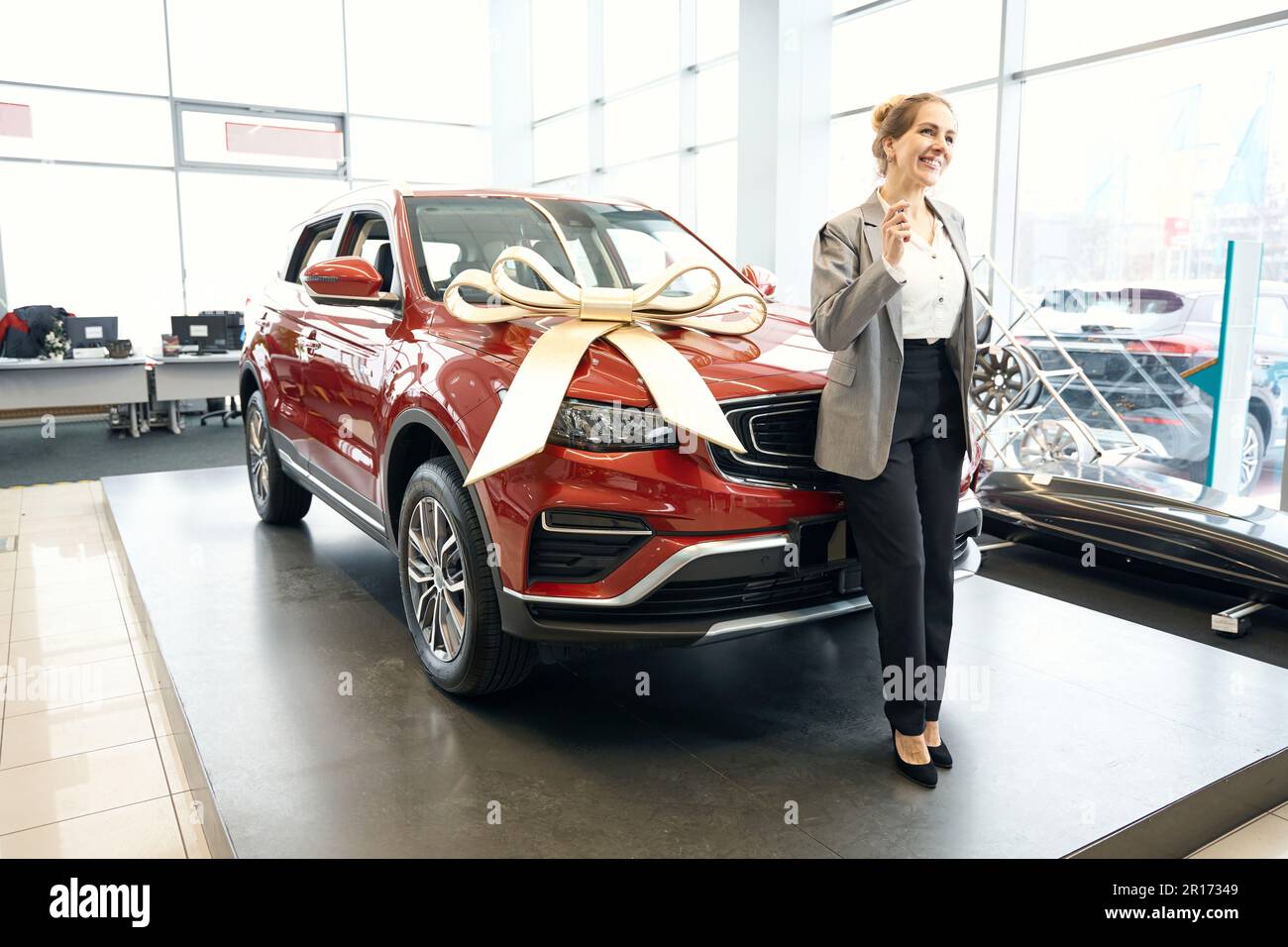 Eine glückliche Frau steht vor einem roten Automobil im Autohaus Stockfoto