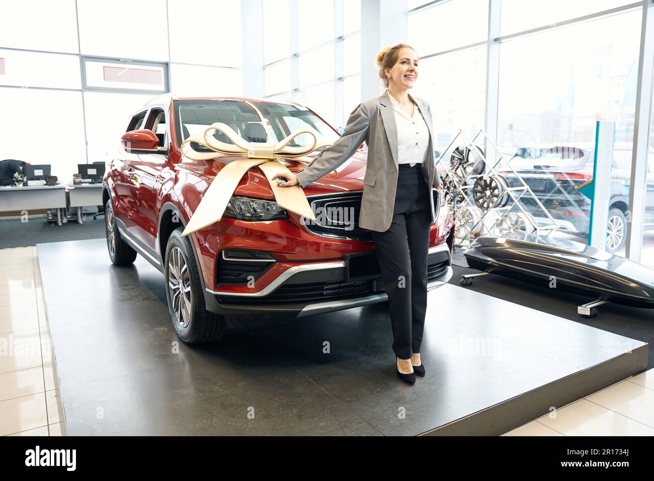 Eine glückliche Frau steht vor einem roten Automobil im Autohaus Stockfoto