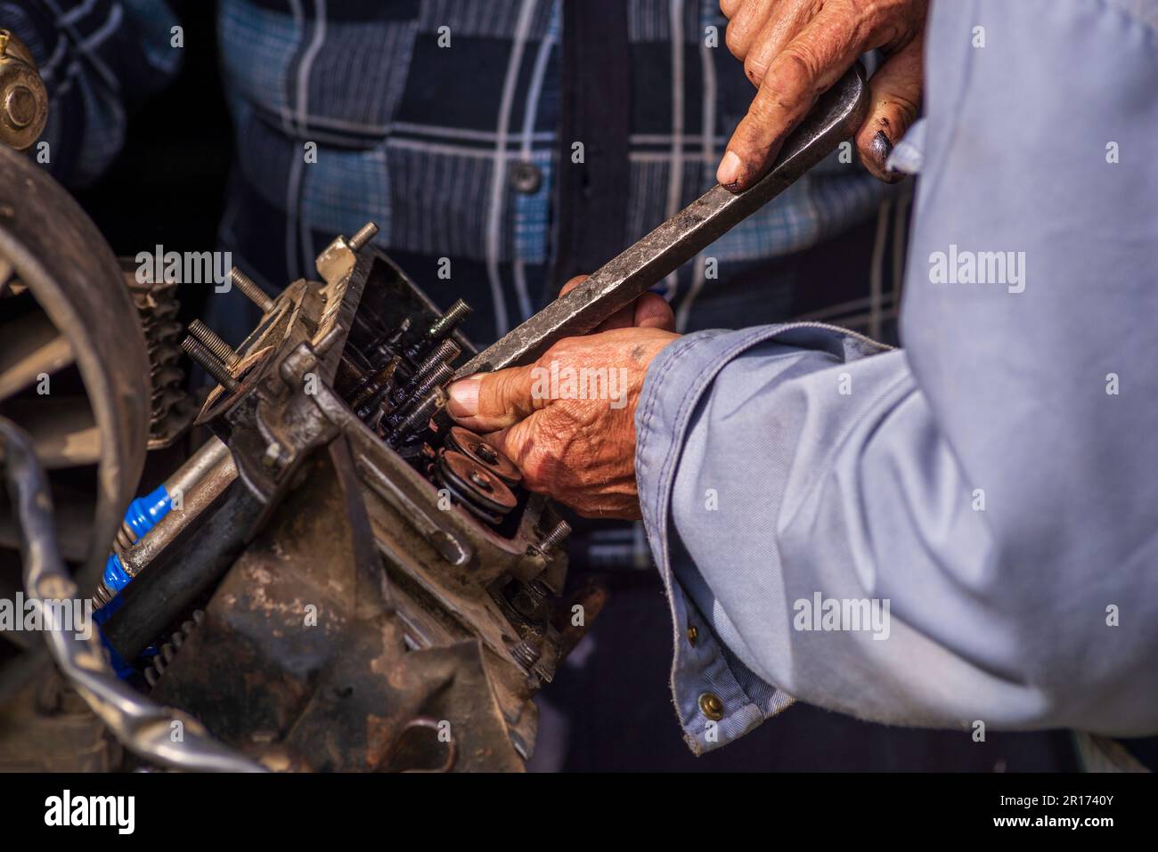 Zwei alte Männer, Automechaniker, die an rostigem Motor arbeiten, in einer Werkstatt. Reparaturservice Nahaufnahme zerknitterte schmutzige Hände blaue Kleidung Gear Truck DISAs Stockfoto