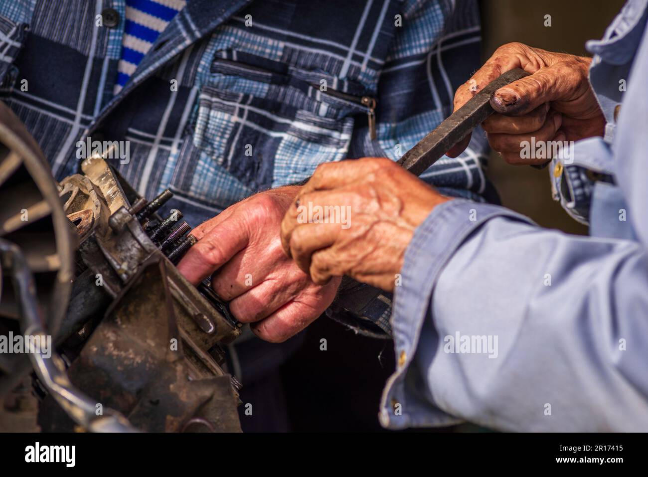 Zwei alte Männer, Automechaniker, die an rostigem Motor arbeiten, in einer Werkstatt. Reparaturservice Nahaufnahme zerknitterte schmutzige Hände blaue Kleidung Gear Truck DISAs Stockfoto