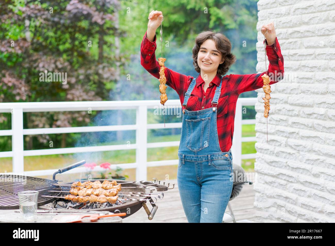 Grillparty im Garten mit einer jungen Frau in Jeansanzug und rotem ...
