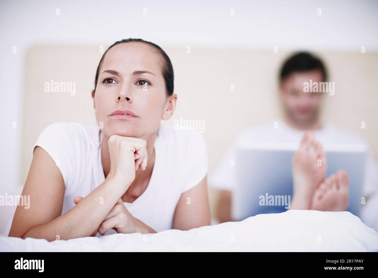 Warum spricht er nicht mit mir... Eine junge Frau, die verärgert über ihren Mann aussieht, der im Hintergrund mit seinem Laptop sitzt. Stockfoto