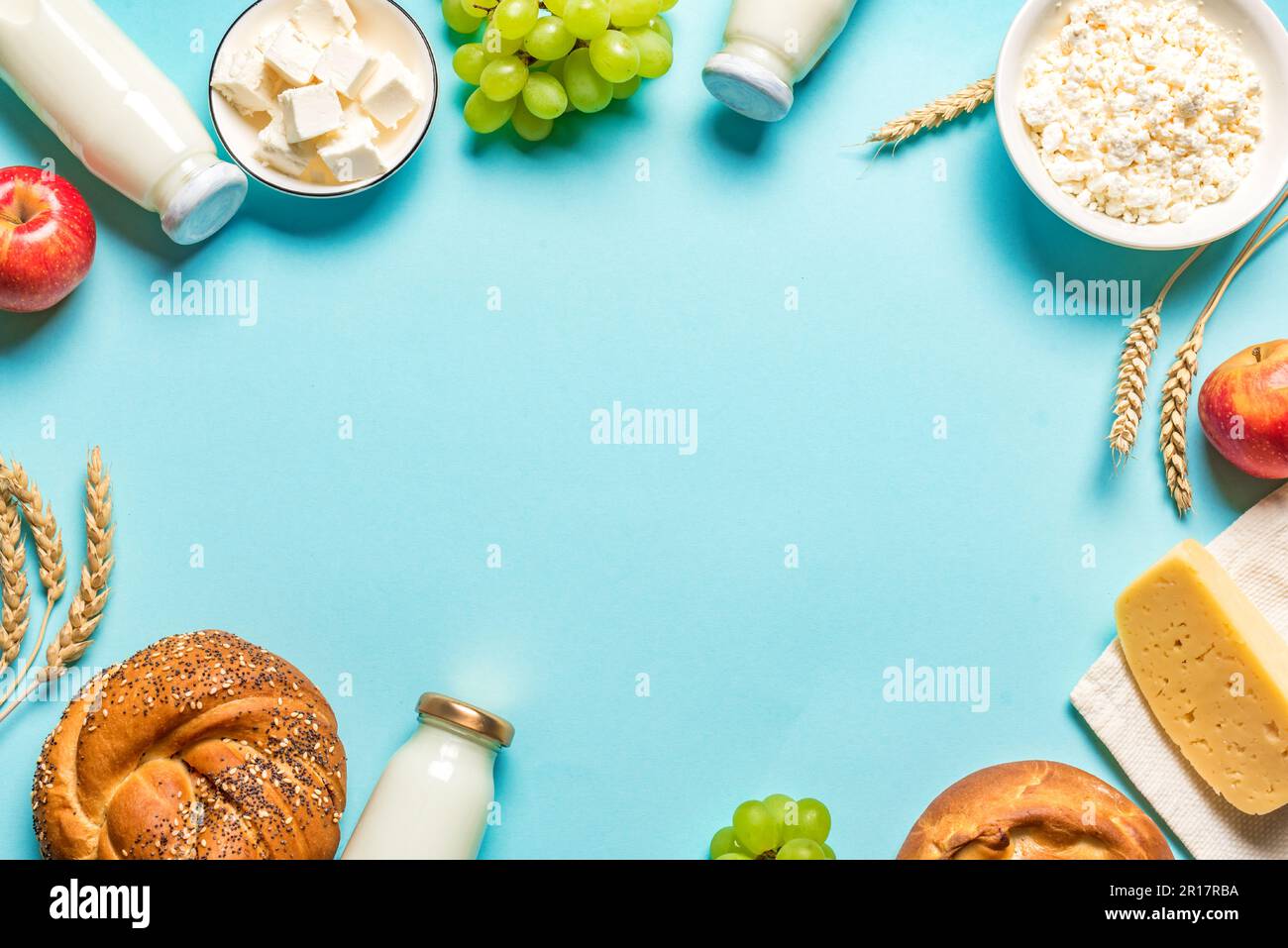 Happy Shavuot - religiöses jüdisches Urlaubskonzept mit Milchprodukten, Käse, traditionellem Brot, Milchflaschen, Weizen und Trauben auf blauem Hintergrund, fr Stockfoto
