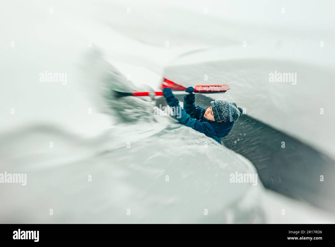 Ein hilfsbereiter Junge, der während eines Schneesturms den Schnee räumt Stockfoto