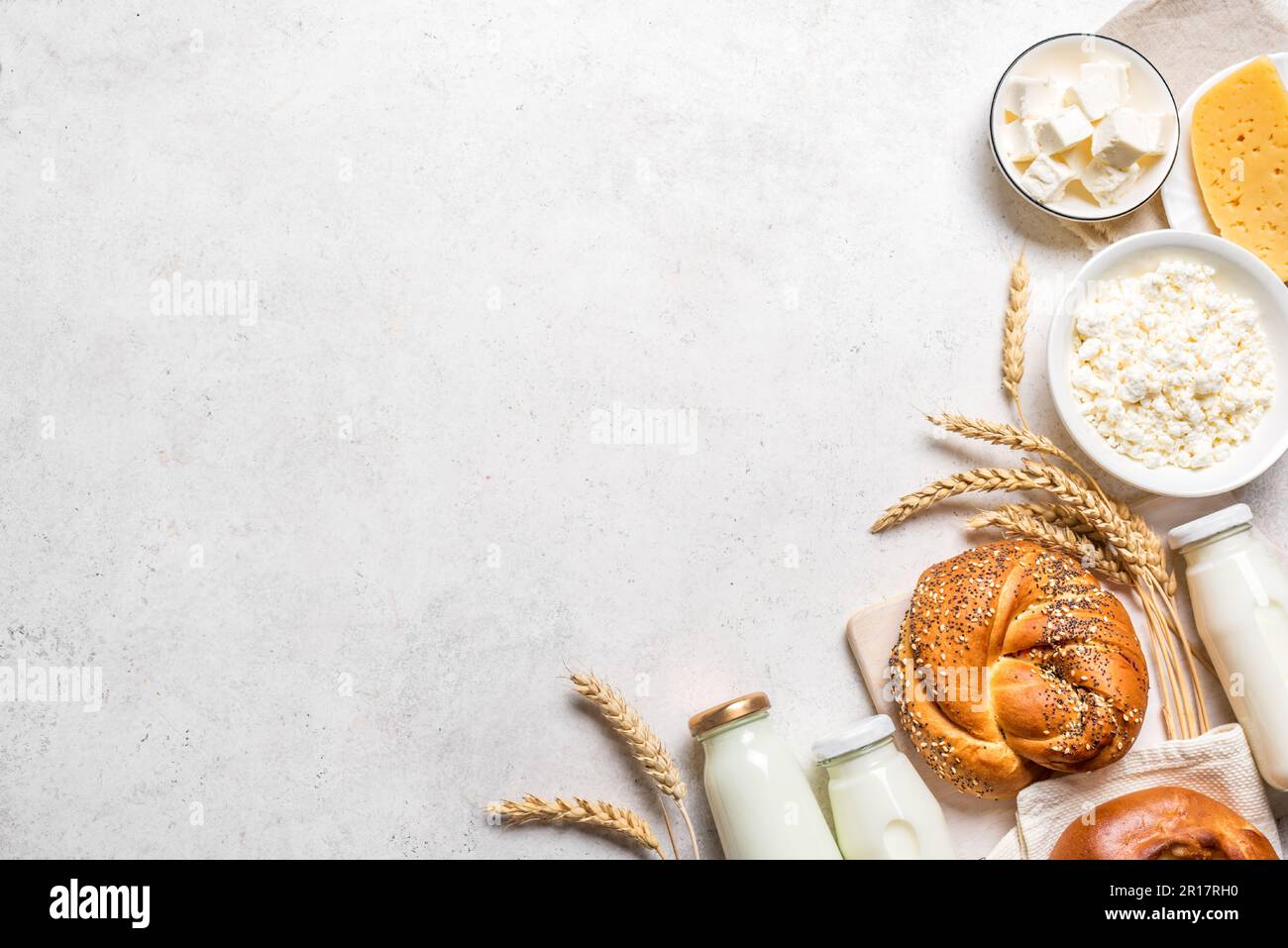 Happy Shavuot - religiöses jüdisches Urlaubskonzept mit Milchprodukten, Käse, traditionellem Brot, Milchflaschen, Weizen auf weißem Hintergrund, Kopierbereich. Stockfoto