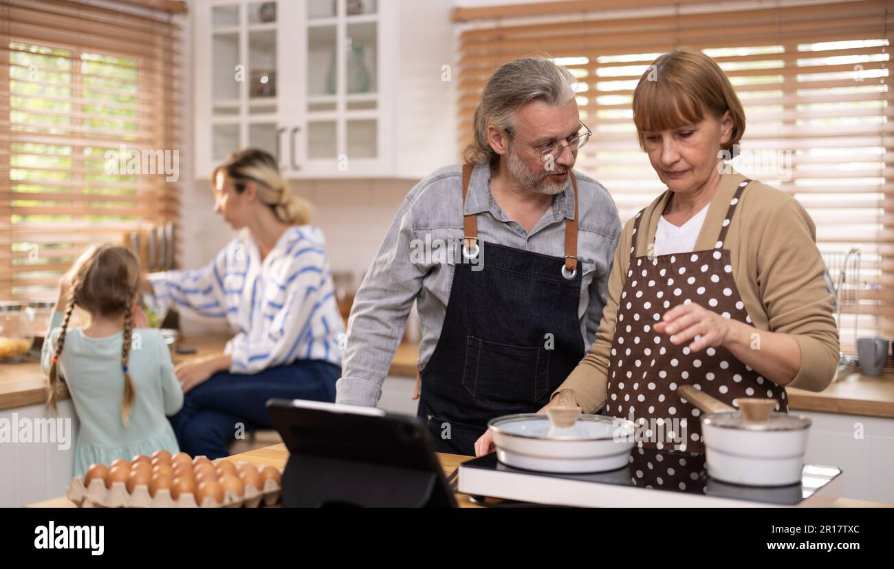 Familienmitglieder aus mehreren Generationen erforschen neue und geschmackvolle Rezepte auf einem Tablet, treffen gesunde Essensauswahl, kochen und genießen Mahlzeiten zusammen. familiengath Stockfoto