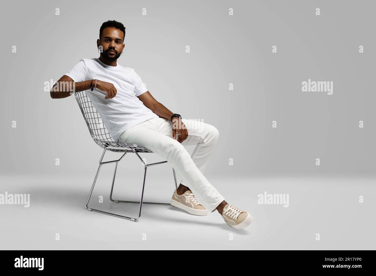 Ein hübscher junger afroamerikanischer Kerl, der auf dem Stuhl sitzt und im Studio posiert - isoliert. Stockfoto
