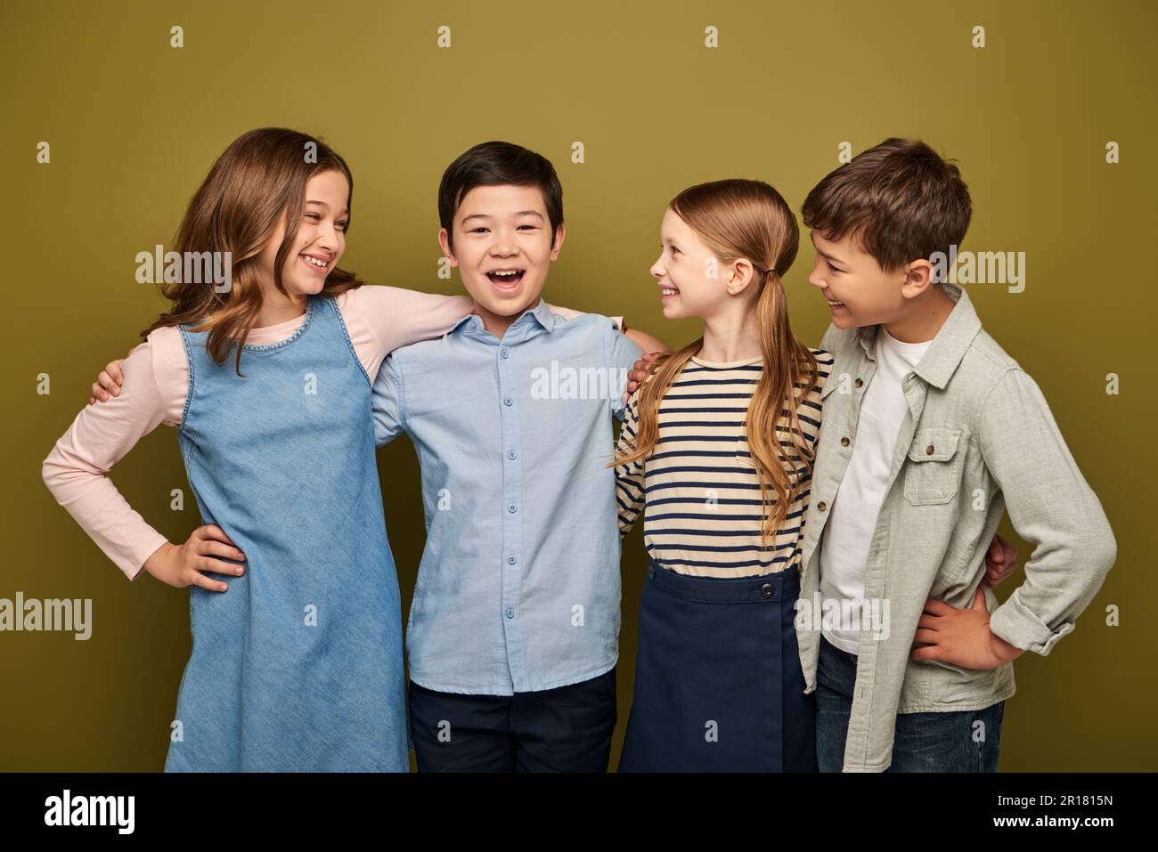 Fröhliche Kinder in lässiger Kleidung, die sich umarmen und asiatischen Freund mit offenem Mund anschauen, während sie den internationalen Kinderschutztag feiern Stockfoto