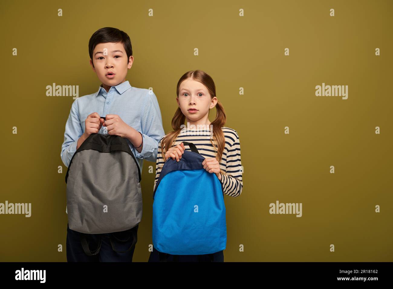 Ängstliche, multiethnische Kinder in lässiger Kleidung, die Rucksäcke in der Hand halten und während des internationalen Kinderschutztags zusammen in die Kamera schauen Stockfoto