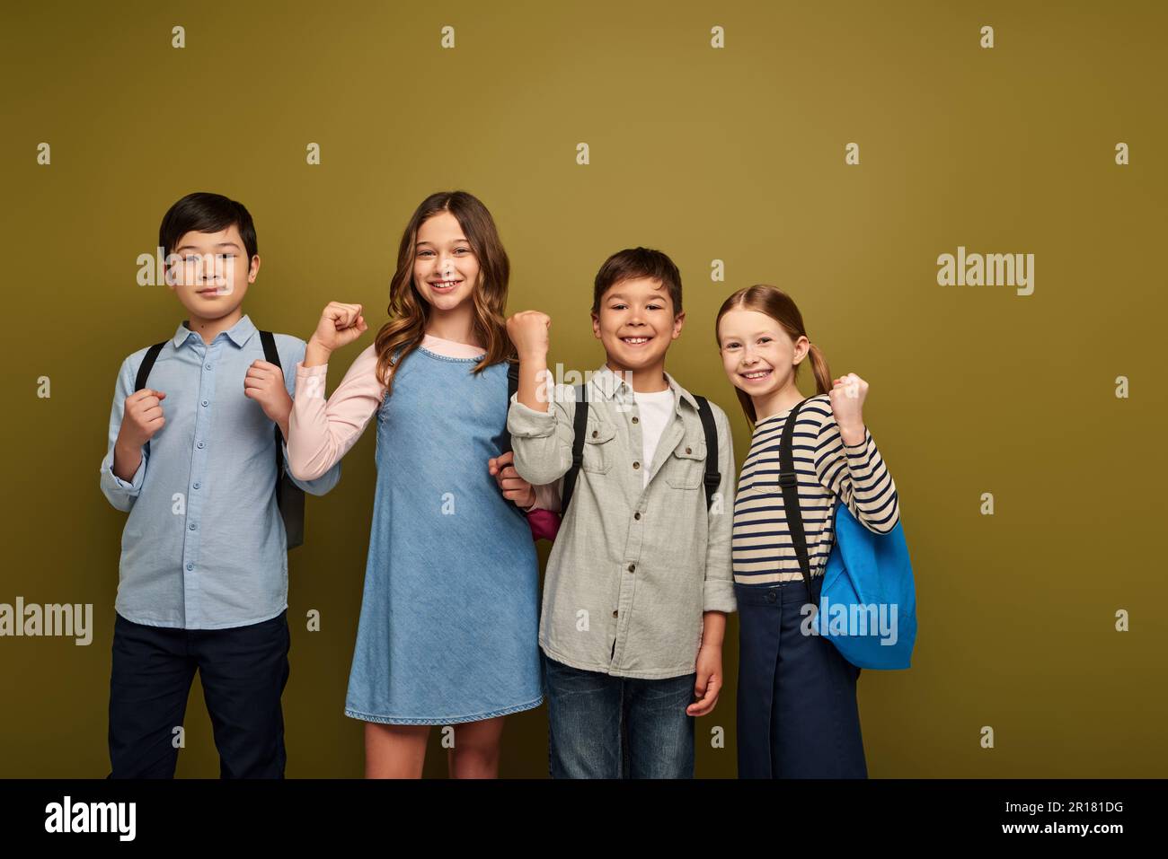 Lächelnde, multiethnische Kinder mit Rucksäcken, die ihre Fäuste als Geste zeigen und während der Feier des Weltkinderschutztages WHI in die Kamera schauen Stockfoto