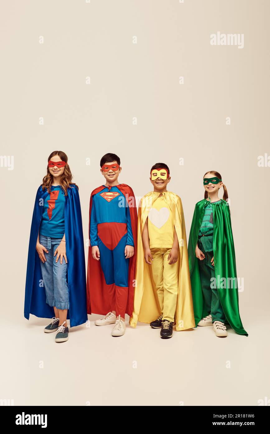 Fröhliche multiethnische Kinder in bunten Superheldenkostümen mit Umhängen und Masken stehen zusammen, während sie den Kinderschutztag Feiertag feiern o Stockfoto