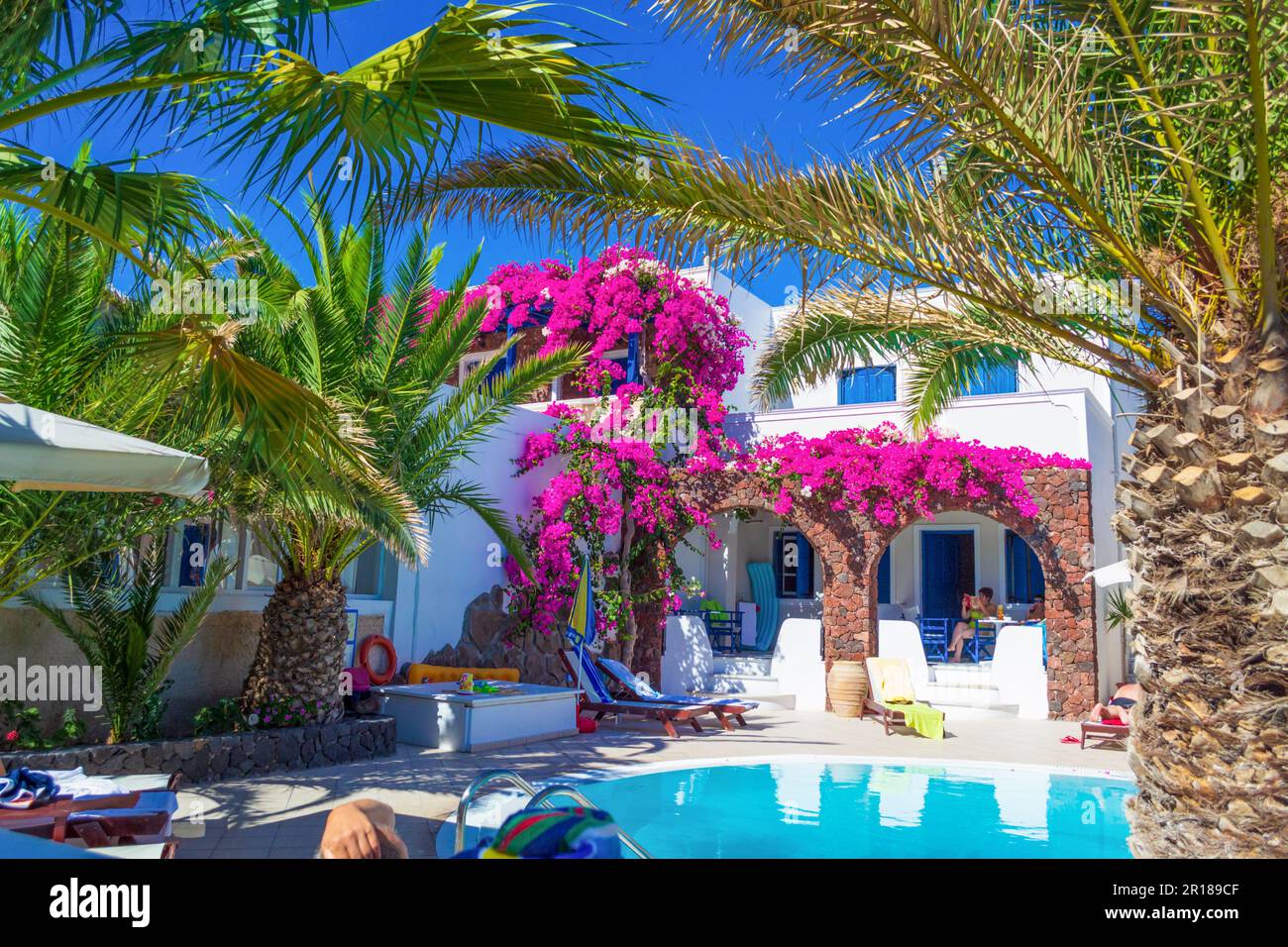 Malerische Terrasse mit blühender rosafarbener Bougainvillea Pflanze, tiefblauem Himmel und gewölbten Dächern - Kamari Dorf Santorini Insel, Griechenland Stockfoto