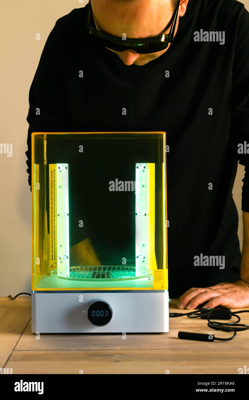 Mann mit Brille, der vor Gebrauch eine Wasch- und Heilungsmaschine mit UV-Licht justiert, für 3D-Harzdrucker Stockfoto