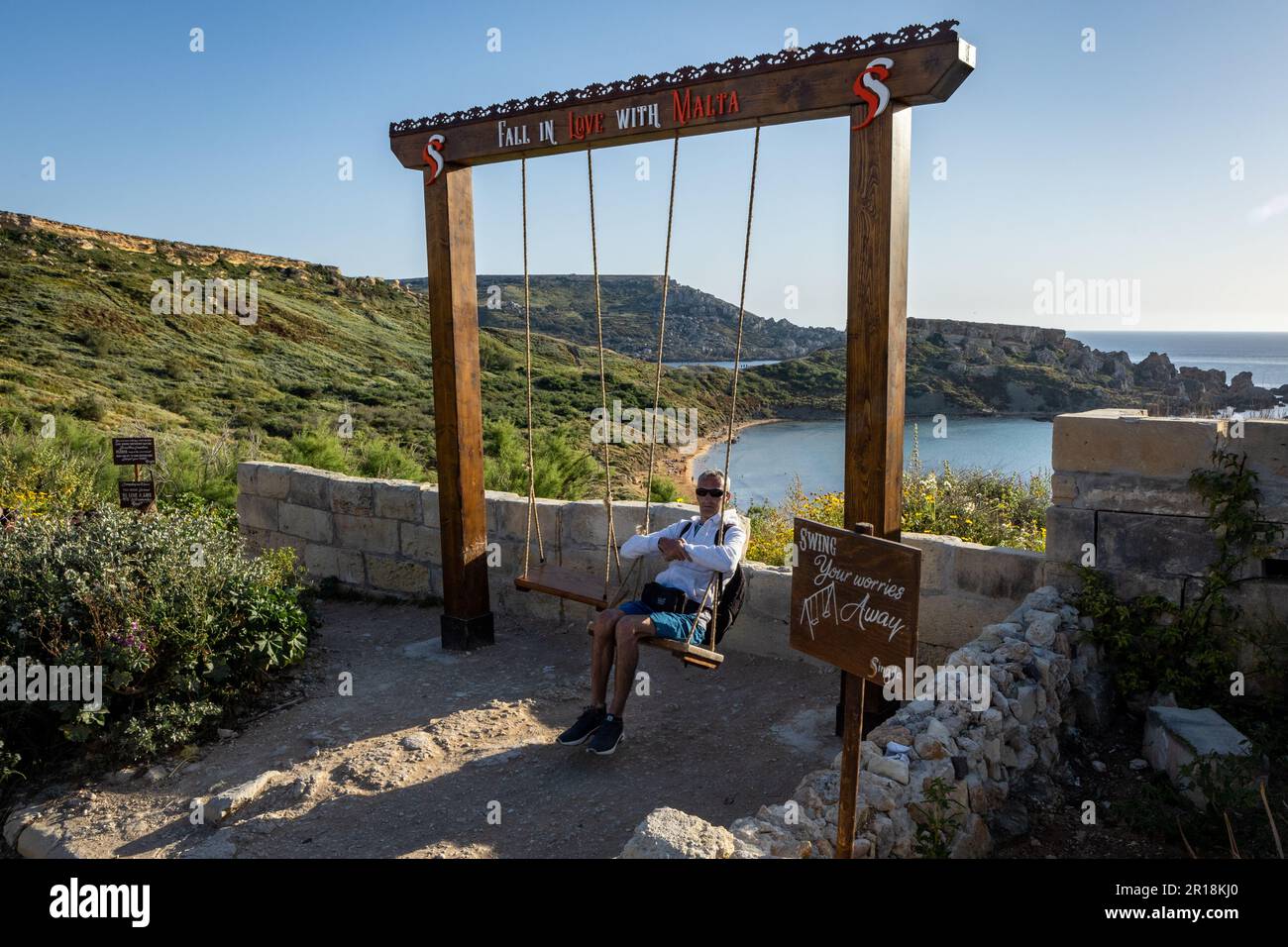 Ghajn Tuffieha, Malta - 17. April 2023: Ein Mann, der sich auf einer hölzernen Schaukel am malerischen Aussichtspunkt des mittelmeers am Singita Miracle Beach erholt. Stockfoto