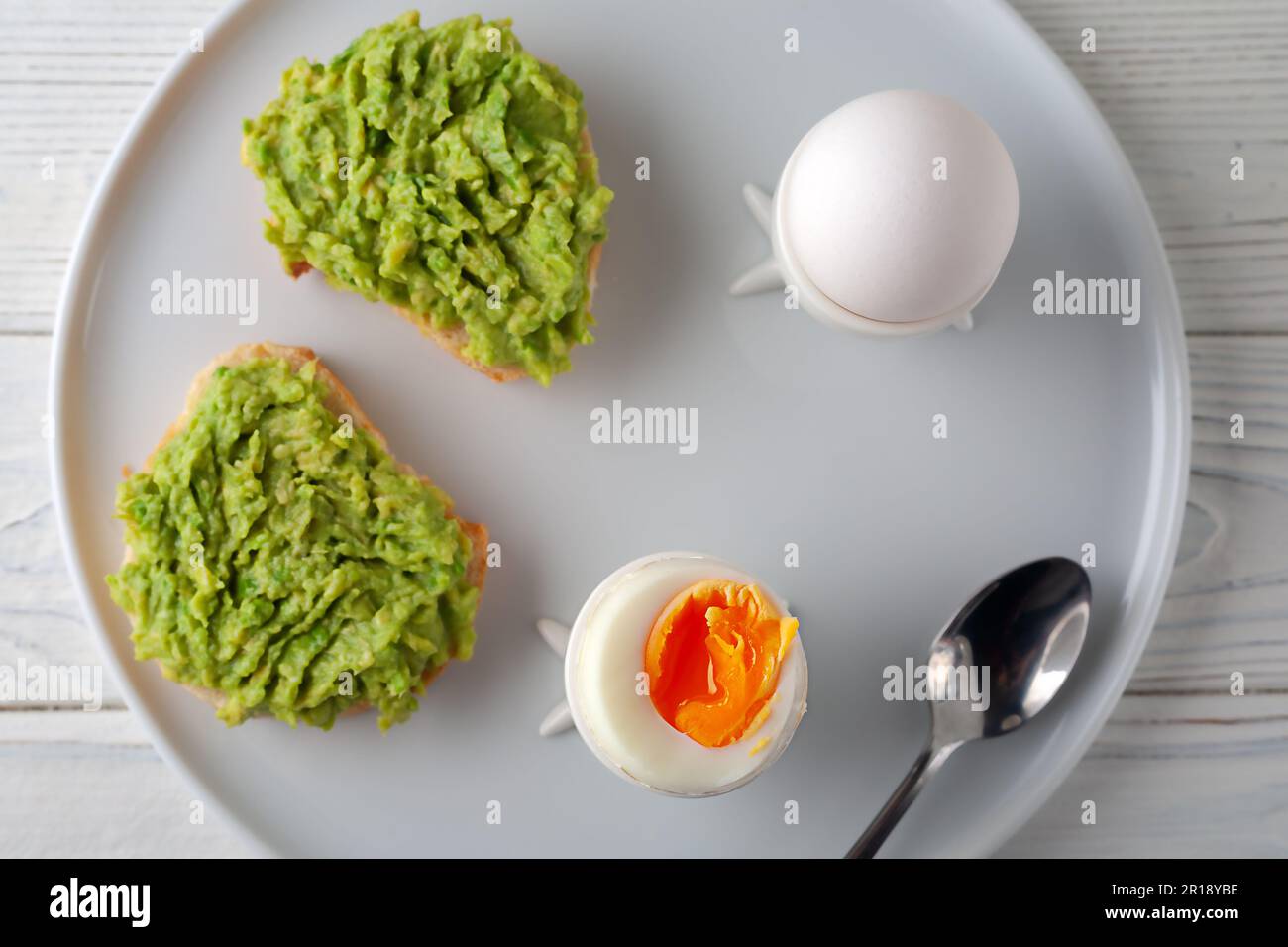 Europäisches Frühstück. Weich gekochtes Ei und offenes Brot-Sandwich mit Avocado auf dem Tisch. Traditionelles Essen für ein gesundes Frühstück. Stockfoto