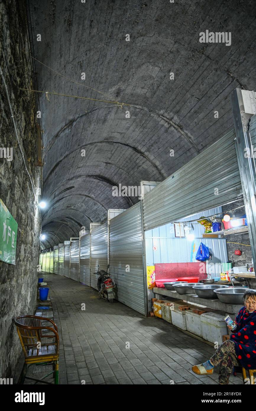 CHONGQING, CHINA - 8. MAI 2023 - das am 8. Mai 2023 aufgenommene Video zeigt einen Lebensmittelmarkt in einem verlassenen Eisenbahntunnel in Chongqing, China. In diesem hundert Meter langen Tunnel sind mehr als 20 Stände nacheinander angeordnet. Die Verkaufsstände sind in feste Verkaufsstände und provisorische Verkaufsstände unterteilt, und die festen Verkaufsstände sind in Fleischbereiche und Bereiche für Wasserprodukte unterteilt. Es wird davon ausgegangen, dass der Tunnel Teil der ehemaligen Eisenbahnlinie des Spezialstahlwerks Chongqing ist, die eine Tunnellänge von etwa 150 Metern hat. Nach dem Bankrott des Spezialstahlwerks Chongqing wurden die einst befahrenen Tunnel allmählich still, A Stockfoto