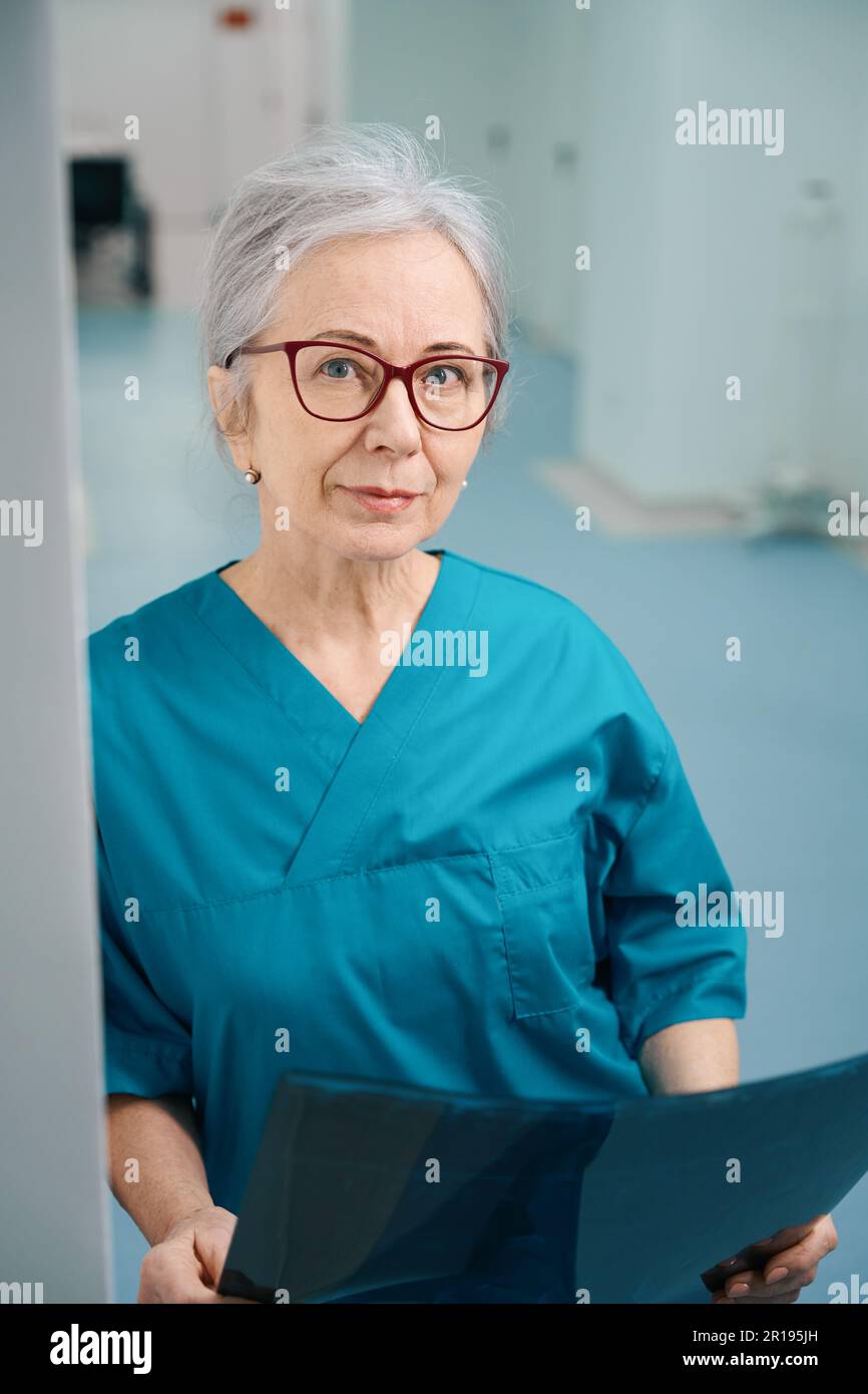 Grauhaarige Sanitäterin steht im Krankenhausgang mit MRT-Scan Stockfoto