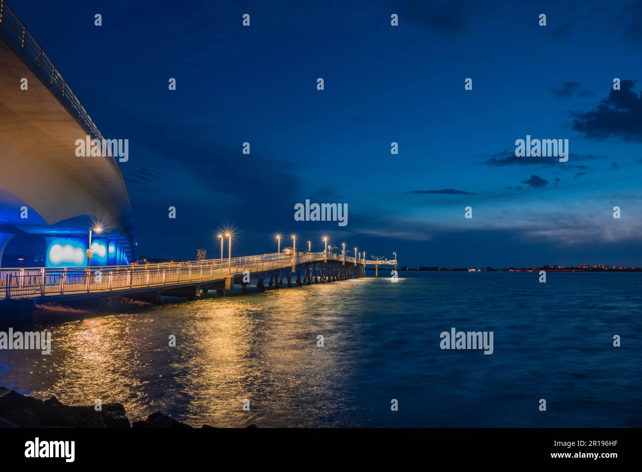 Sarasota, FL, USA-10. April 2023: Angelpier in Sarasota Bay mit Ringling Bridge im Hintergrund am Abend zu blauen Zeiten mit dramatischem Himmel. Stockfoto