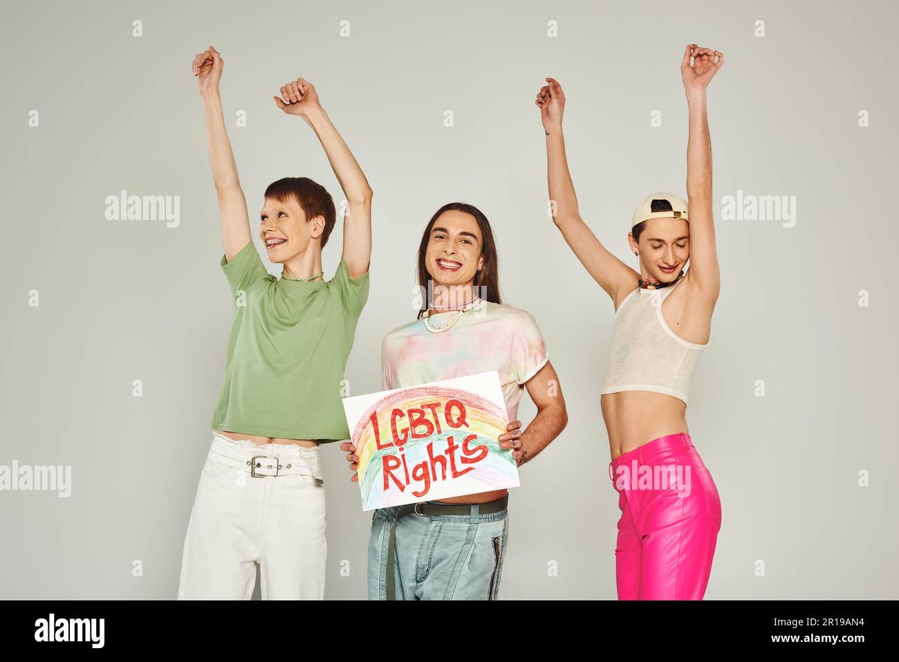 Fröhliche lgbt-Freunde in farbenfrohen Kleidern, die mit erhobenen Händen neben einem Plakat mit lgbtq-Rechten und einem Lächeln auf dem Stolz mon tanzen Stockfoto