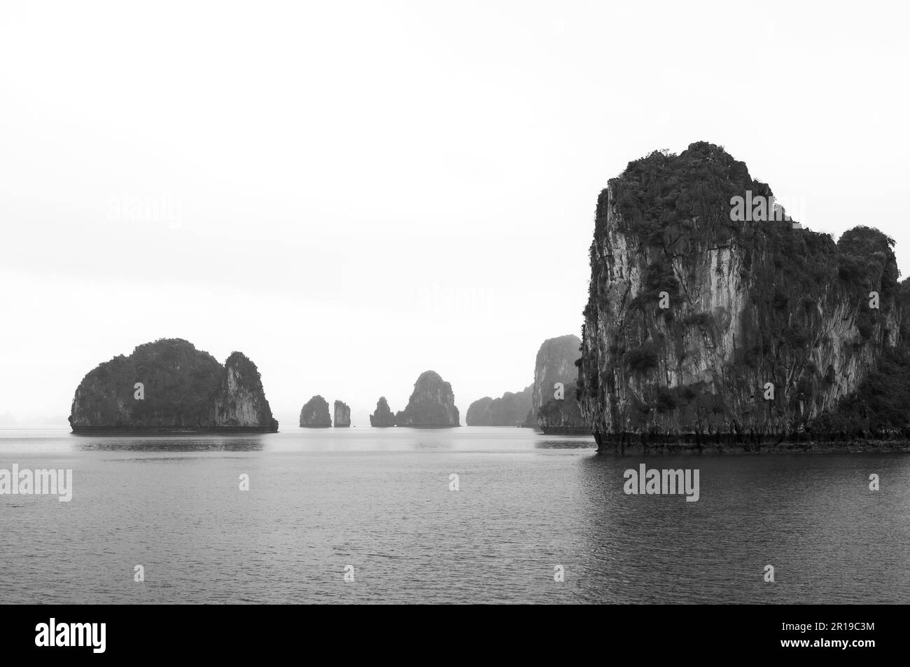 Die typischen Kalksteininseln und Inseln in niedrigen Wolken und Nebel in der Bai TU Long Bay, Halong Bay, Vietnam. Stockfoto