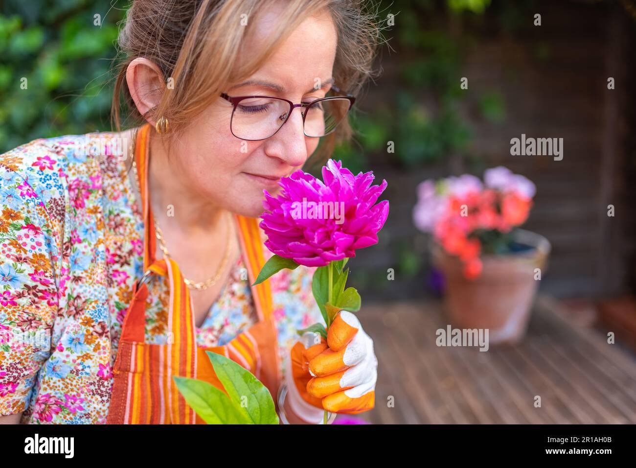 Reife Frau, die eine Blume riecht, während sie im Frühling den Garten ihres Hauses anlegt Stockfoto