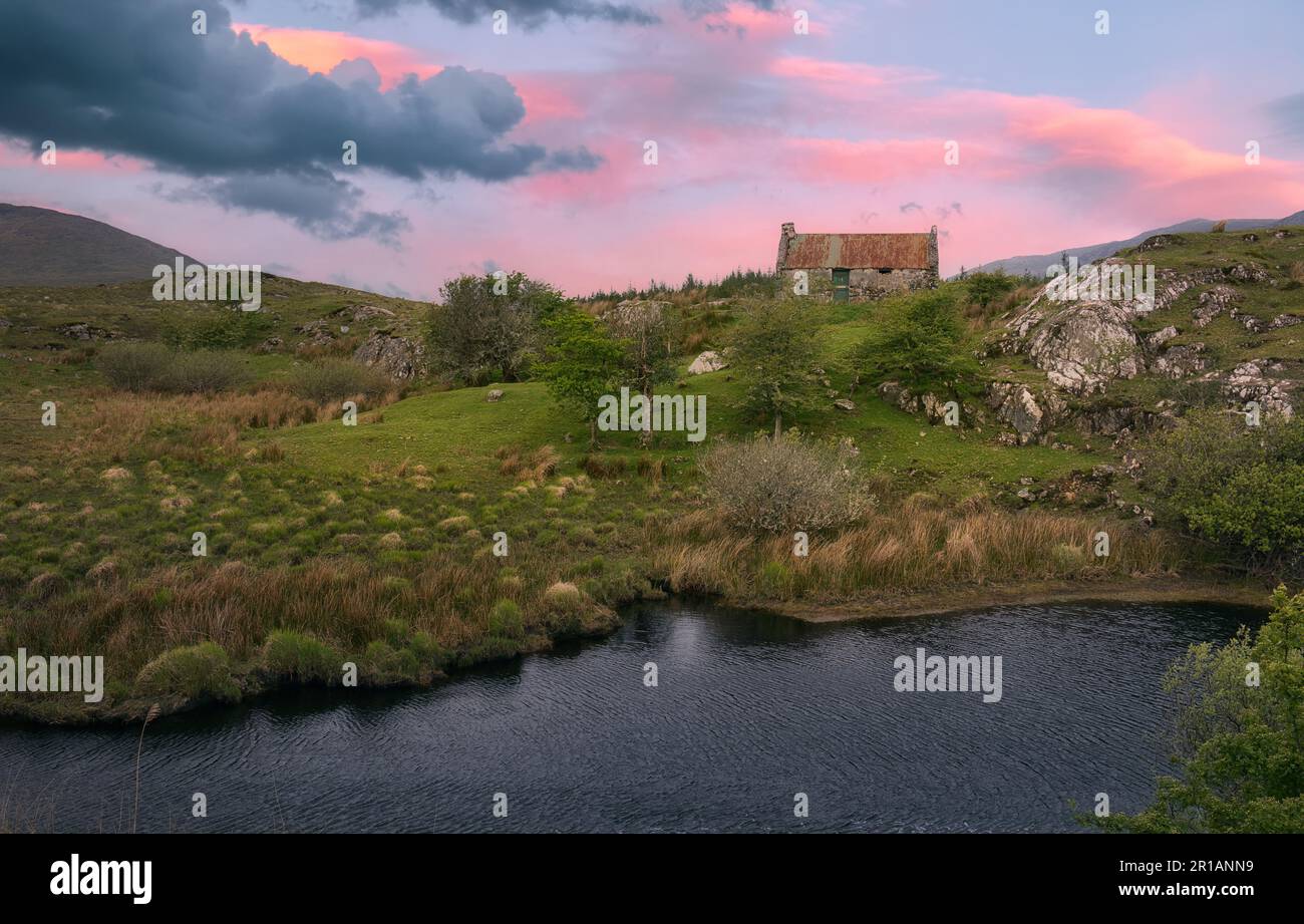 Wunderschöne Landschaft bei Sonnenaufgang mit einem alten rostigen Dachhaus am Fluss mit Bergen im Hintergrund im Connemara National Park in Grafschaft Galway, Irland Stockfoto