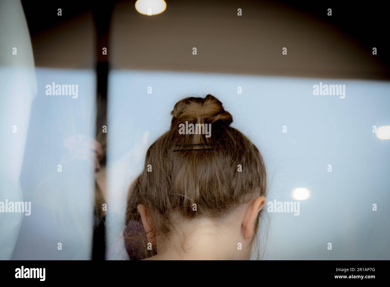 Hinterkopf des Mädchens, Haare im Brötchen, durch ein Fenster gucken Stockfoto