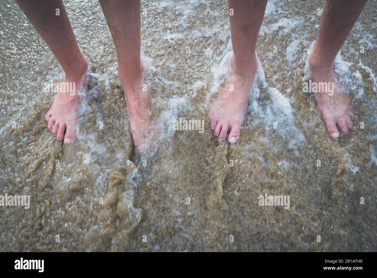 Zwei Paar Kinderfüße auf dem Sand im Wasser. Familie auf Urlaub. Füße und Sandkörner. Stockfoto