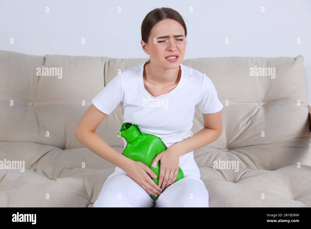 Junge Frau, die zu Hause eine Wärmflasche benutzt, um Zystitisschmerzen auf dem Sofa zu lindern Stockfoto