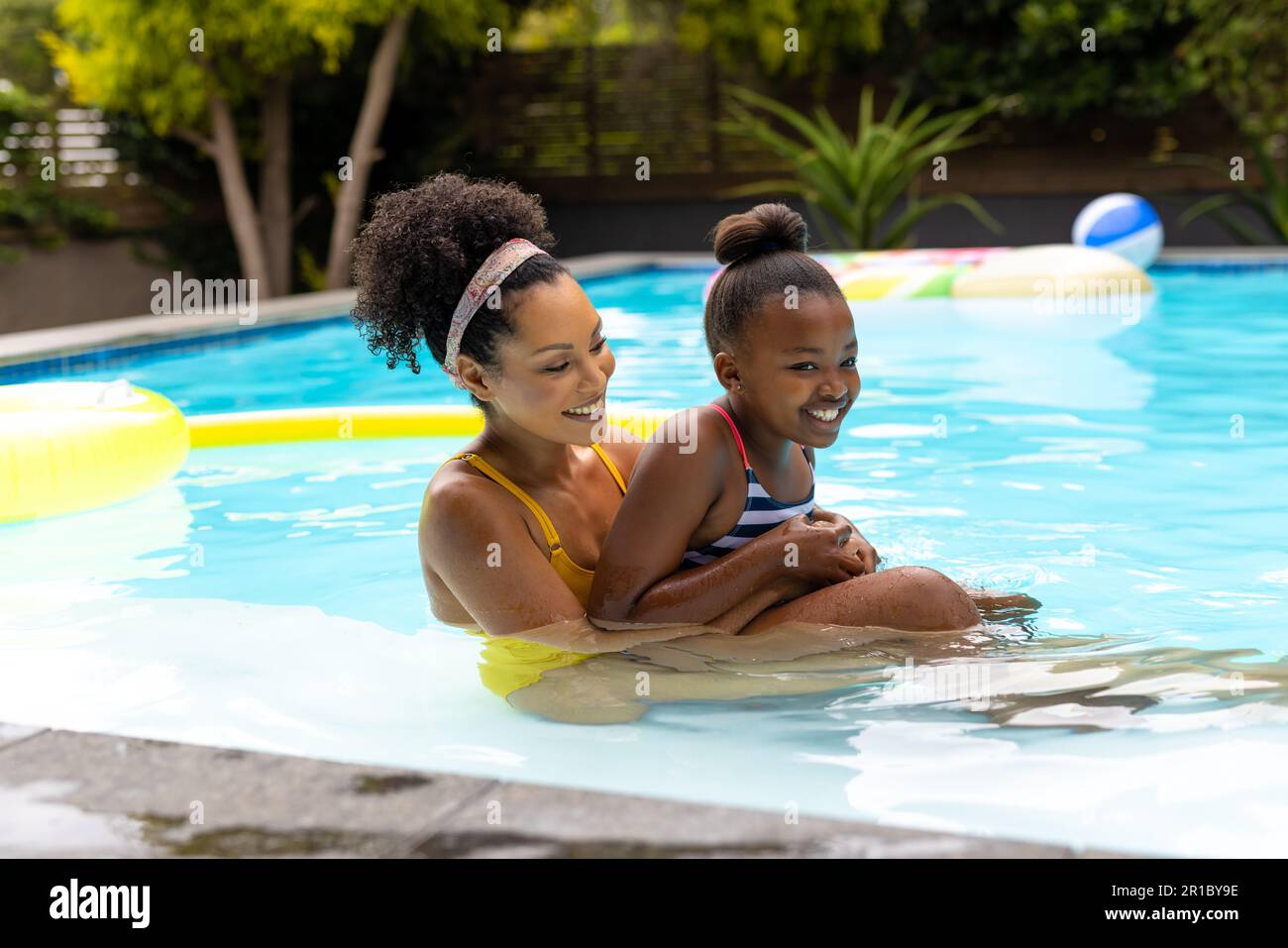 Glückliche afroamerikanische Mutter und Tochter, die Spaß zusammen haben, sich im Swimmingpool zu umarmen Stockfoto