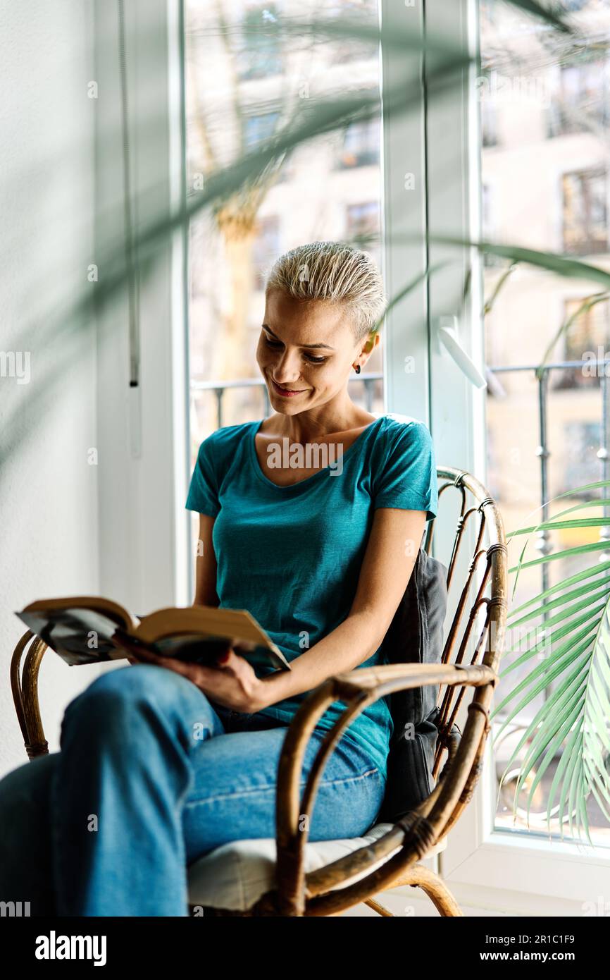 Stilvolle Frau, die ein Buch liest und zu Hause lächelt Stockfoto