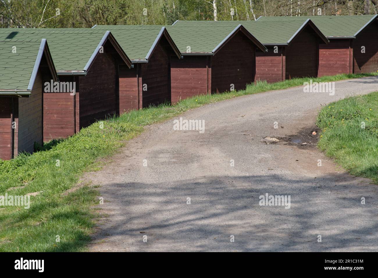 Eine Reihe hölzerner Sommerferienhäuser entlang einer staubigen Landstraße in der tschechischen Landschaft. Billige Ferienwohnungen in Waldhütten. Stockfoto