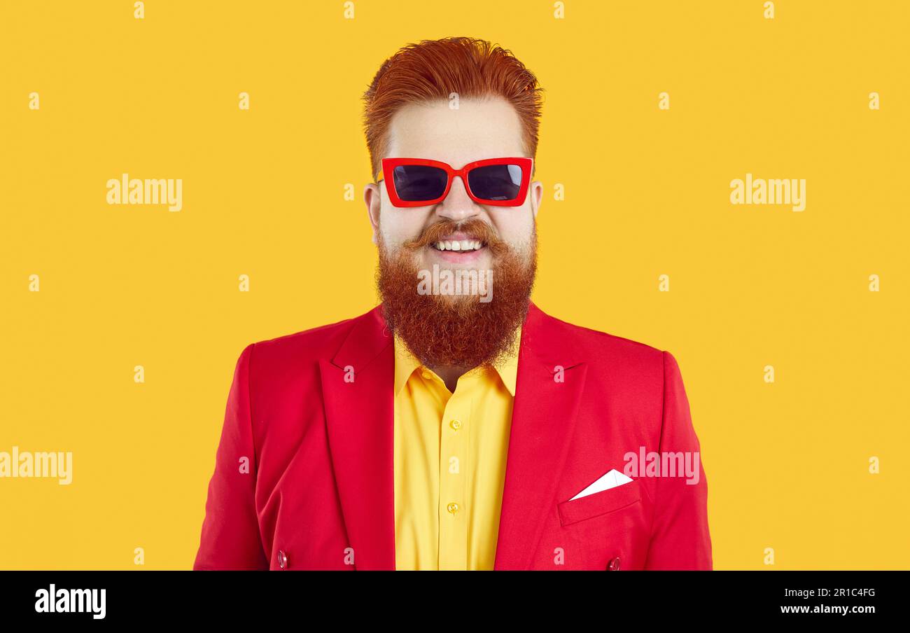 Studio-Porträt eines fröhlichen, lustigen, bärtigen, fetten Typen in rotem Anzug, gelbem Hemd und cooler Sonnenbrille Stockfoto