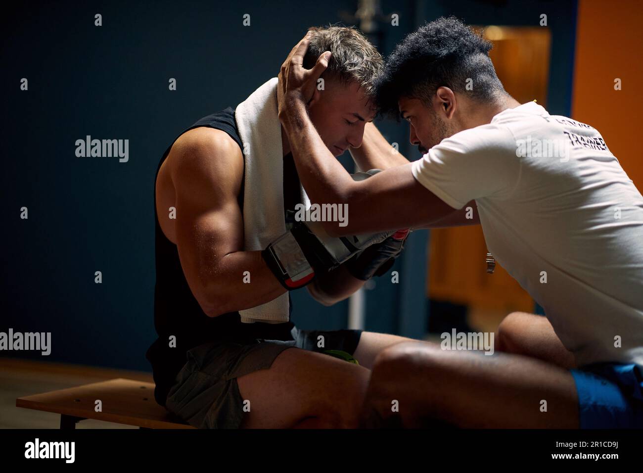Der Trainer hilft dem jungen Boxspieler dabei, sich mental vorzubereiten, seinen Kopf zu halten und mit ihm zu sprechen, in der Garderobe, die auf einer Bank sitzt. Sport, Kampfsport, Leben Stockfoto